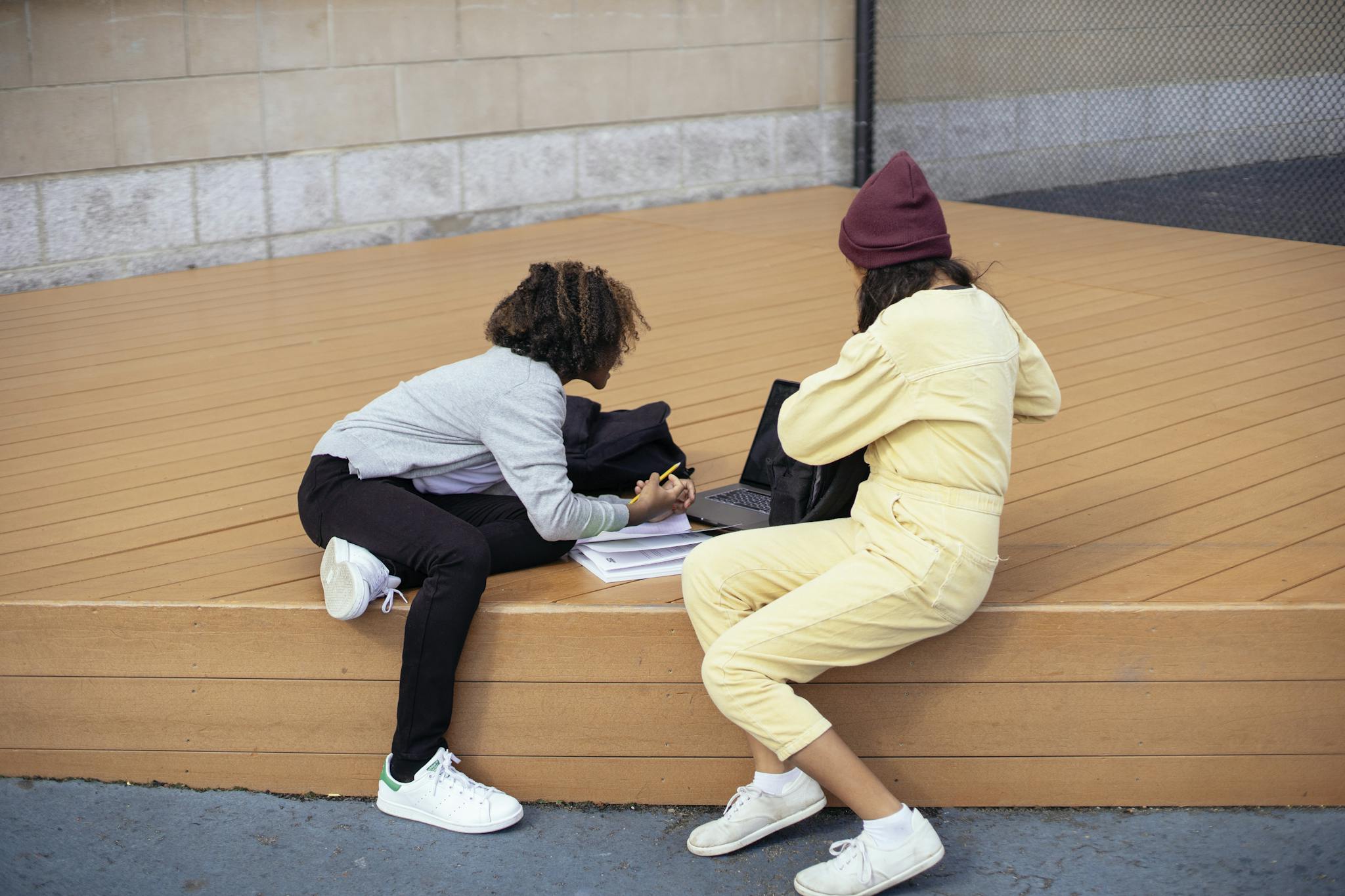 Unrecognizable multiethnic schoolgirls sharing laptop while studying on street